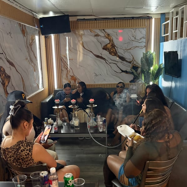 Group of women enjoying hookah and food at Island Grill AZ, with marble and wood paneling.