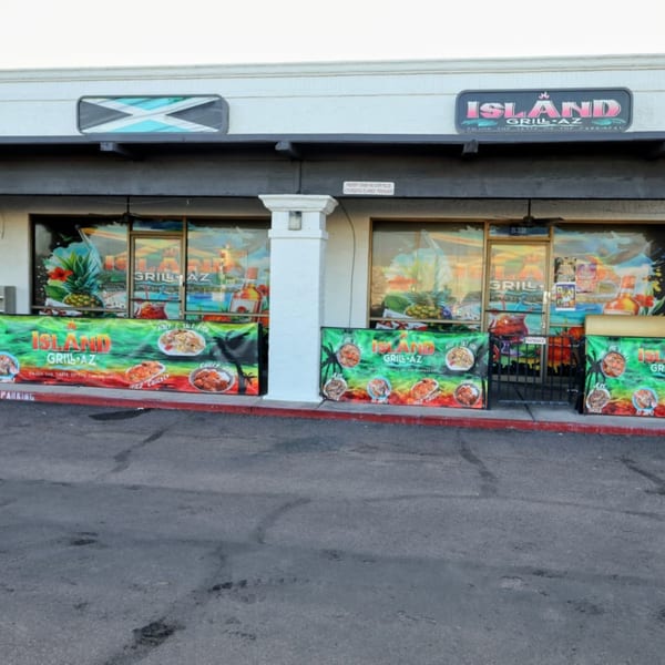 Exterior of Island Grill AZ with Jamaican flag, colorful banners, and tropical window decals.