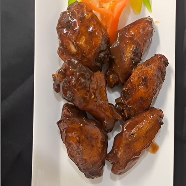 Six Jamaican jerk chicken wings, glazed with a dark sauce, on a white rectangular plate.