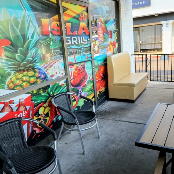 Outdoor patio seating at Island Grill AZ with a colorful window mural and a tan booth.