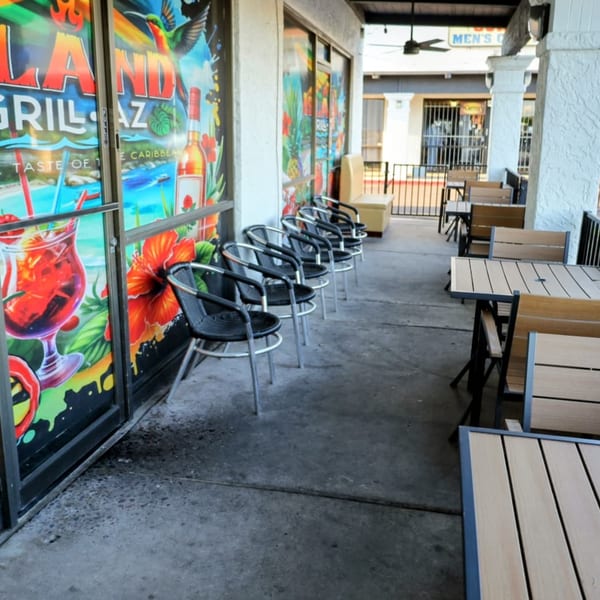 Island Grill AZ's outdoor patio with colorful window murals, black chairs, and wooden tables.