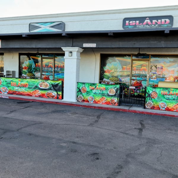 Exterior of Island Grill AZ, a Jamaican restaurant, with colorful banners displaying menu items.