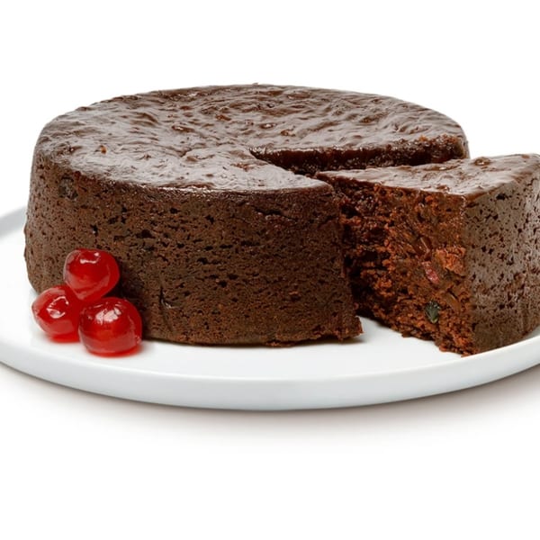 A Jamaican rum fruit cake with a slice removed, garnished with three red cherries.