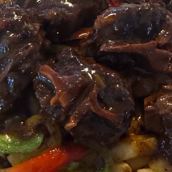 Close-up of Jamaican oxtail stew with bell peppers and potatoes from Island Grill AZ.