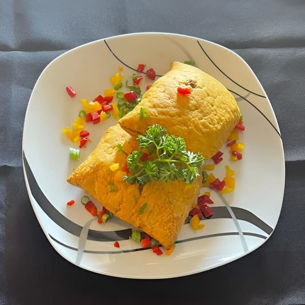 Two golden Jamaican patties garnished with parsley and colorful bell peppers on a white plate.