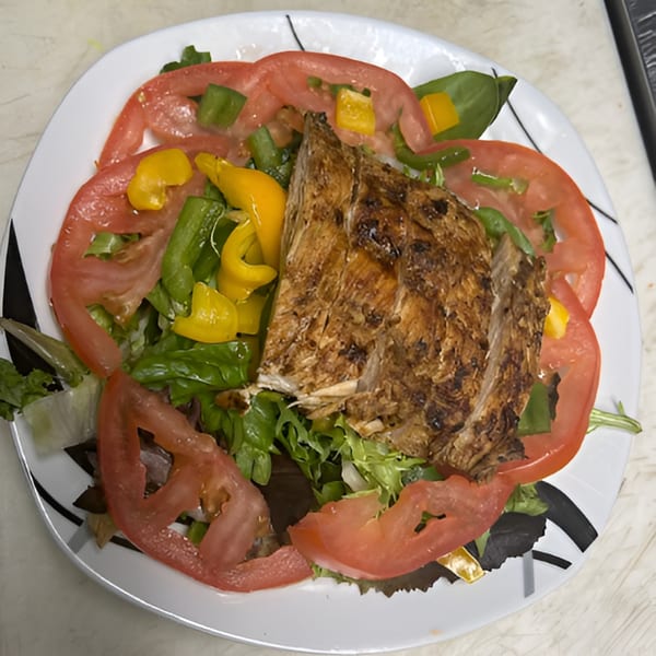 Grilled jerk chicken on a bed of mixed greens with sliced tomatoes and bell peppers.