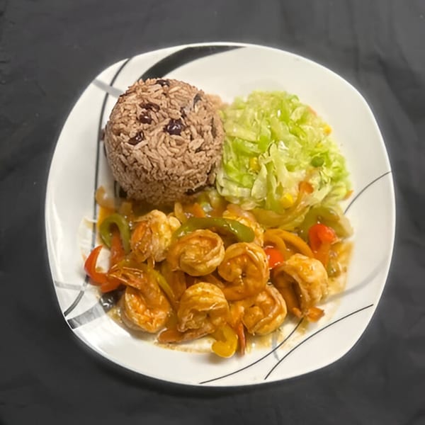 Jamaican curry shrimp with bell peppers, rice and peas, and shredded cabbage on a white plate.