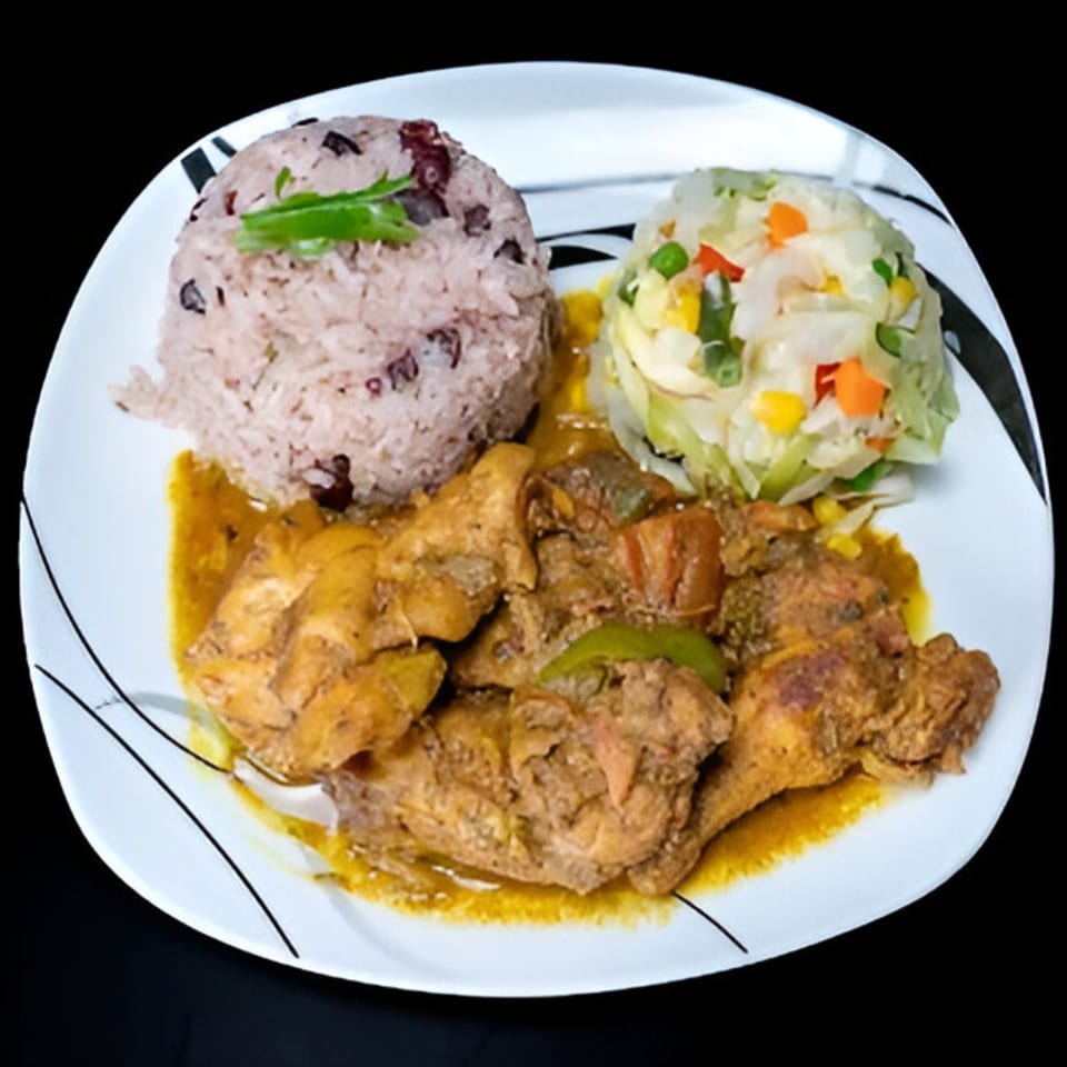Curried chicken with rice and peas, and mixed vegetables on a white plate.