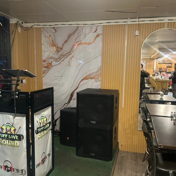 DJ equipment and speakers set up in a Jamaican restaurant dining area with tables and a bar.
