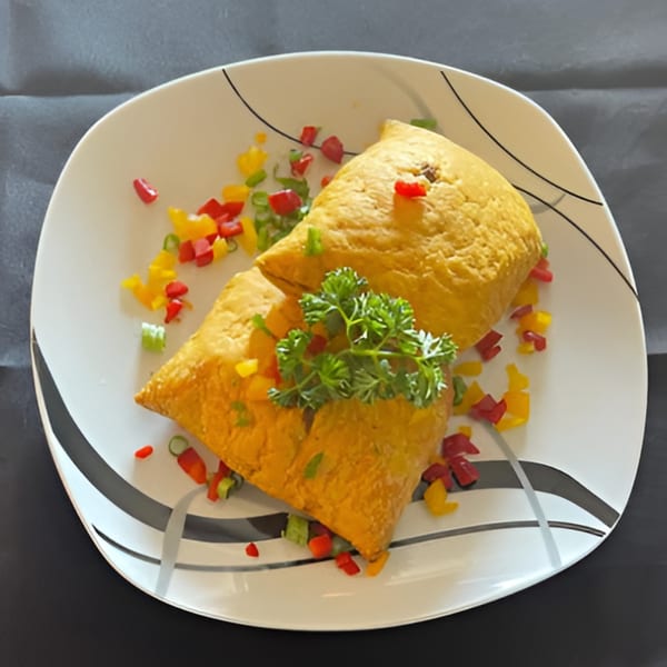 Two golden Jamaican patties garnished with parsley and colorful diced bell peppers on a white plate.