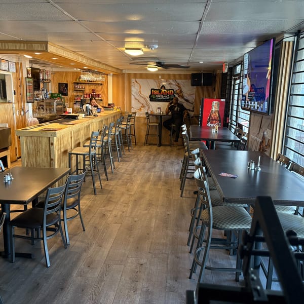 Interior of Island Grill AZ, showing a wooden bar, dining tables, and a man seated at a high-top table.
