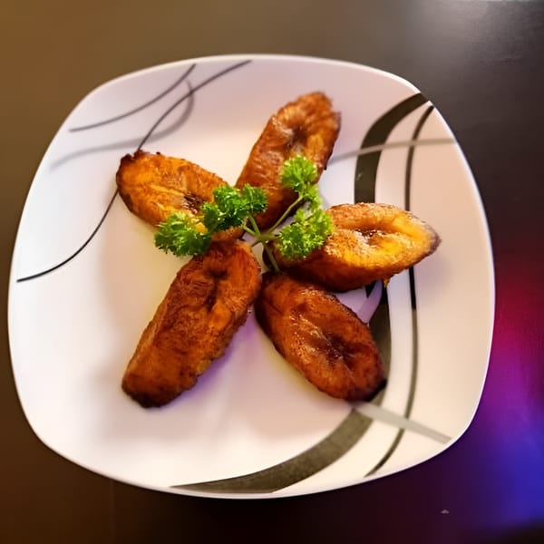 Five golden-brown fried plantains arranged in a star shape with parsley on a white plate.
