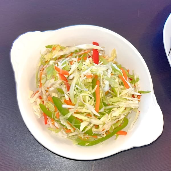 A white bowl filled with a colorful coleslaw of shredded cabbage, carrots, and bell peppers.