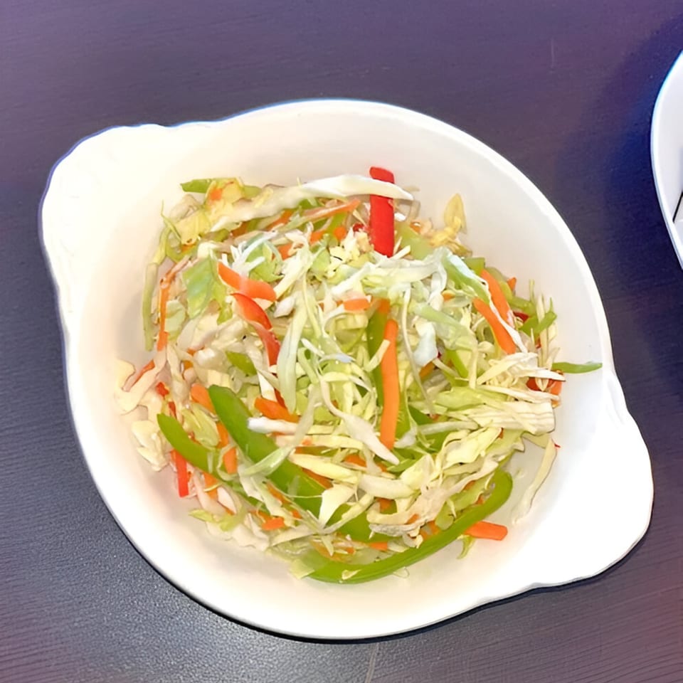 A white bowl filled with a colorful coleslaw of shredded cabbage, carrots, and bell peppers.