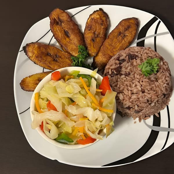 A Jamaican meal with fried plantains, rice and peas, and steamed cabbage on a white plate.
