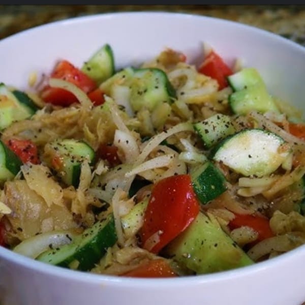 Close-up of a Jamaican salad with cucumbers, tomatoes, and onions, seasoned with black pepper.